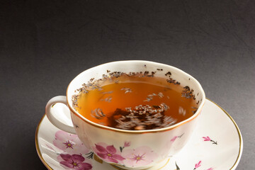 Close up view of tea cup isolated on a black background. Tea leaves on the surface of the water.