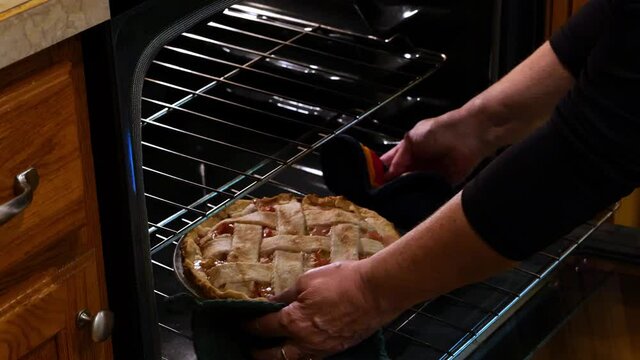 Woman hands taking delicious hot rhubarb custard pie with lattice crust from the oven.