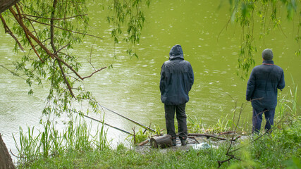 Fishing in the rain. Fisherman in a raincoat by the lake.