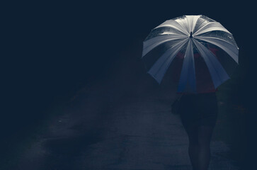 A woman walks down the night street with an umbrella.