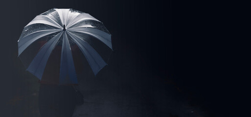 A woman walks down the night street with an umbrella.