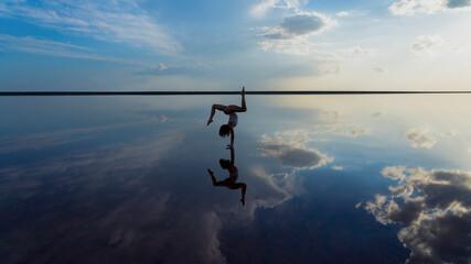 flexible girl stands on her arms in the mirror water of a salt lake.hand balance among the clouds