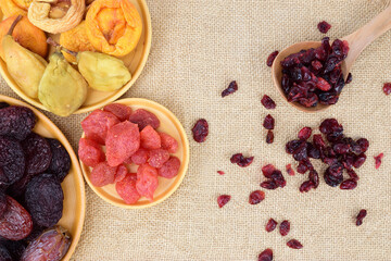 Top view of several plates of dried fruit and a wooden spoon with dried lingonberries scattered on the table