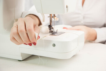 Girl sews cotton white fabric on the sewing machine. Close-up.
