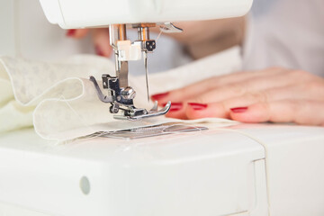 Girl sews cotton white fabric on the sewing machine. Close-up.
