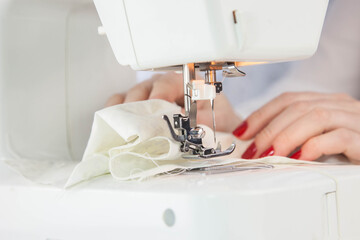Girl sews cotton white fabric on the sewing machine. Close-up.
