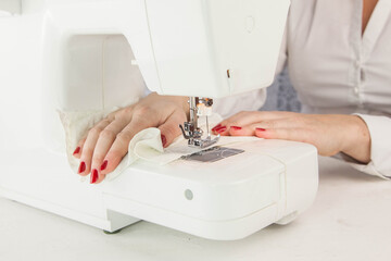 Girl sews cotton white fabric on the sewing machine. Close-up.
