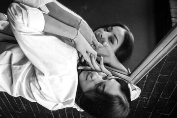 young pretty girl with long hair in a white shirt lies on the mirror, dark room. She is lying on her hands looking at the camera. Low key, sloping horizon 