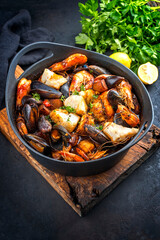 Traditional French seafood bouillabaisse with fish, king prawns and mussels in tomato sauce as close-up on a modern design pot