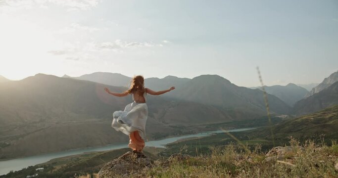 Woman in white dress running on a mountain with raised hands while wind is blowing her dress and red hair - freedom, nature concept 4k footage