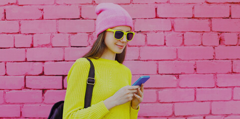 Portrait of young woman with phone in the city over a pink wall background