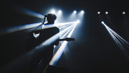 Silhouette of guitar player performinf on concert stage. Dark background, smoke, concert  spotlights