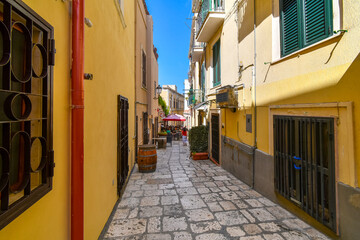 Obraz premium A woman walks down a colorful narrow alley towards a cafe in the Italian city of Brindisi Italy, in the Puglia region.