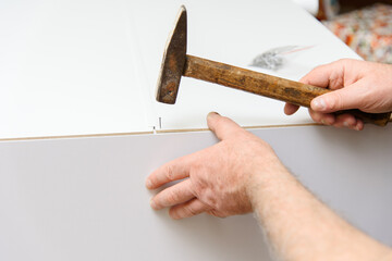 Hands holding a hammer and hammering in nails assembling wooden furniture