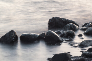 Long exposure of sea and rocks. Boulders sticking out from smooth wavy sea. Tranquil scene.