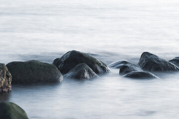 Long exposure of sea and rocks. Boulders sticking out from smooth wavy sea. Tranquil scene.