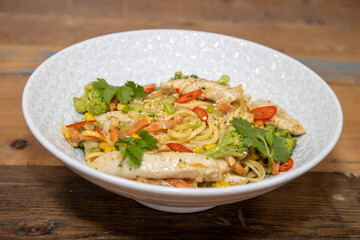 A top down view of a plate of delicious stir-fry ginger and peanut chicken noodle in a white bowl in a kitchen