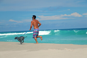 man running on the beach with his pitbull dog