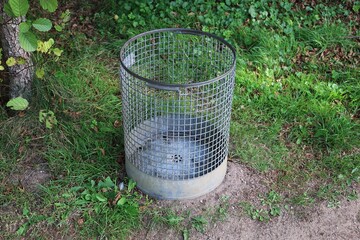 empty metallic trash can is standing in the park