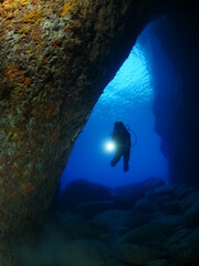 Scuba divers underwater exploring lightcaves blue ocean scenery with torch 
