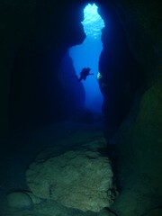 Scuba divers underwater exploring lightcaves blue ocean scenery with torch 
