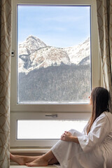 Woman in a bathrobe looking out of the window of her hotel room at Lake Louise, Canada