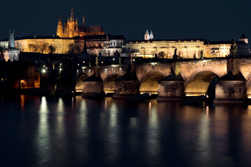 Obraz premium prague castle and charles bridge and st. vita church lights from street lights are reflected on the surface of the vltava river in the center of prague at night in the czech republic
