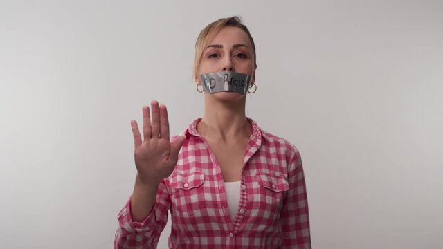 Young woman with mouth taped writing no racism.Woman with tape in her mouth with no message to racism on white background. Message given silently. No racism.