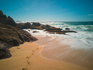 Fototapeta na wymiar Rocas en la orilla del mar con pisadas en la arena que salen del agua