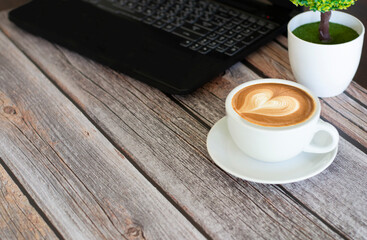 Hot latte coffee laying near the notebook on wooden table, working space 