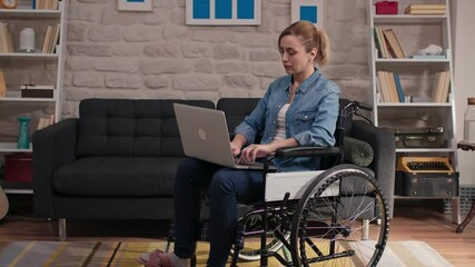 Disabled woman working alone with laptop in a wheelchair at home.Home study concept.A disabled woman working alone with laptop in a wheelchair in the living room at home.