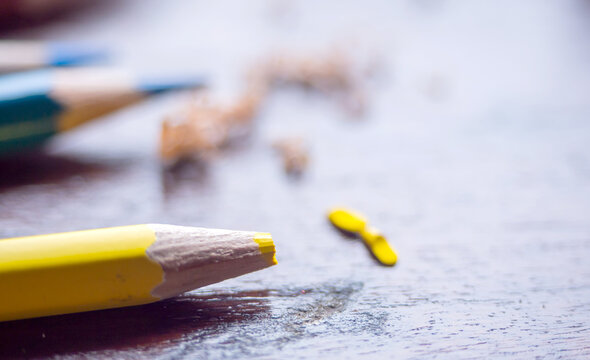 yellow broken color pencil on wooden table in blurry blue sharped pencil at background. artistic idea, develop art in aducation concept. colorful art wallpaper