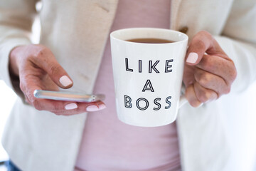 Business woman using mobile phone and holding cup that says Like A Boss