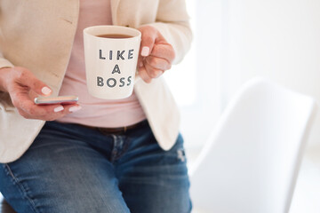 Business woman sitting on top of a table using mobile phone and holding cup that says Like A Boss