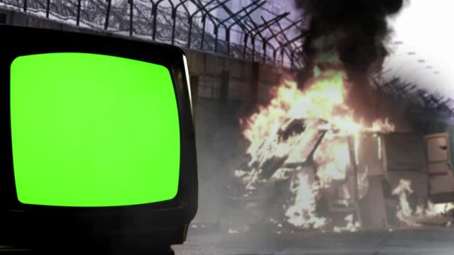 Old Television Green Screen near a Barbed Wire Wall and Burning Van in the Background. Dolly Shot. You can replace green screen with the footage or picture you want. 4K Resolution.