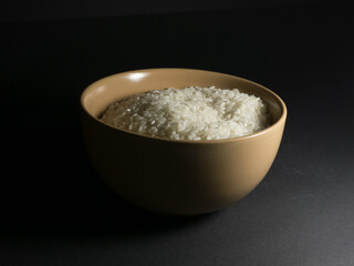 White uncooked rice in a bowl with scattered grains nearby on a black background