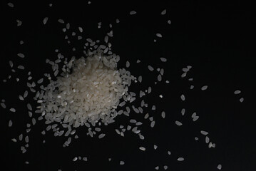 Obraz na płótnie Canvas Scattered white uncooked rice in cereals on a black background