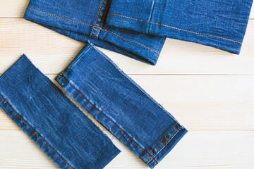 Cut pieces of long denim pants on a wooden background.