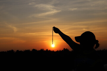 A woman with a chain hanging from the sunset Above the treetops