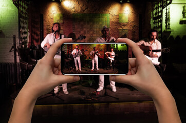 Woman with smartphone taking photo of musicians in a nightclub 