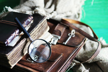 Old leather bag with a magnifying glass on a brown traveler wooden table background with copy space.
