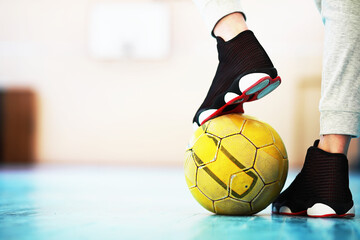 A human foot rest on the football on the concrete floor. Photo of one soccer ball and sneakers in a...