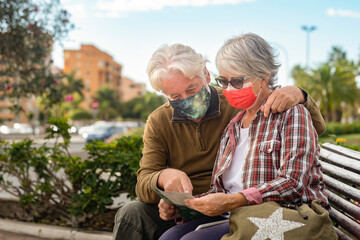 White-haired traveler couple consults a map during the city tour, wearing a surgical mask due to the coronavirus. Active retired people enjoying travel and freedom