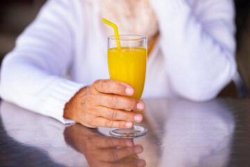 Natural orange juice in the hands of a senior woman sitting at the cafe table