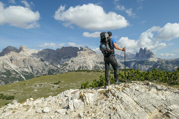Man with a big hiking backpack and distant view on Drei Zinnen from Strudelkopf in Italian...