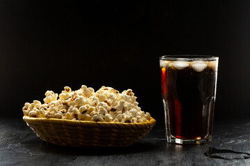 Popcorn and soda with ice cubes on black background