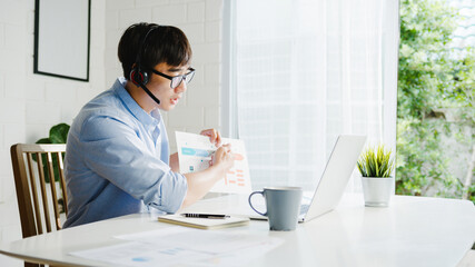 Young Asia businessman using laptop talk to colleagues about plan in video call while smart working from home at living room. Self-isolation, social distancing, quarantine for corona virus prevention.