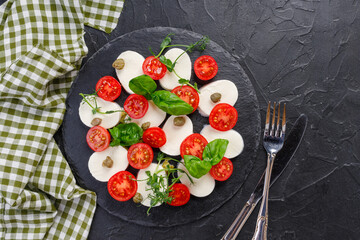 traditional caprese salad on a dark plate. Tomatoes with mozzarella cheese with basil on a dark background.