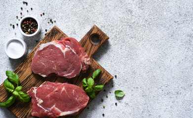 Raw cooking Ribeye beef steak with basil on a wooden board. View from above