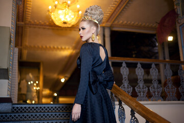 Gorgeous young blonde female model, dressed in a long black dress with bow at the back, elegant...